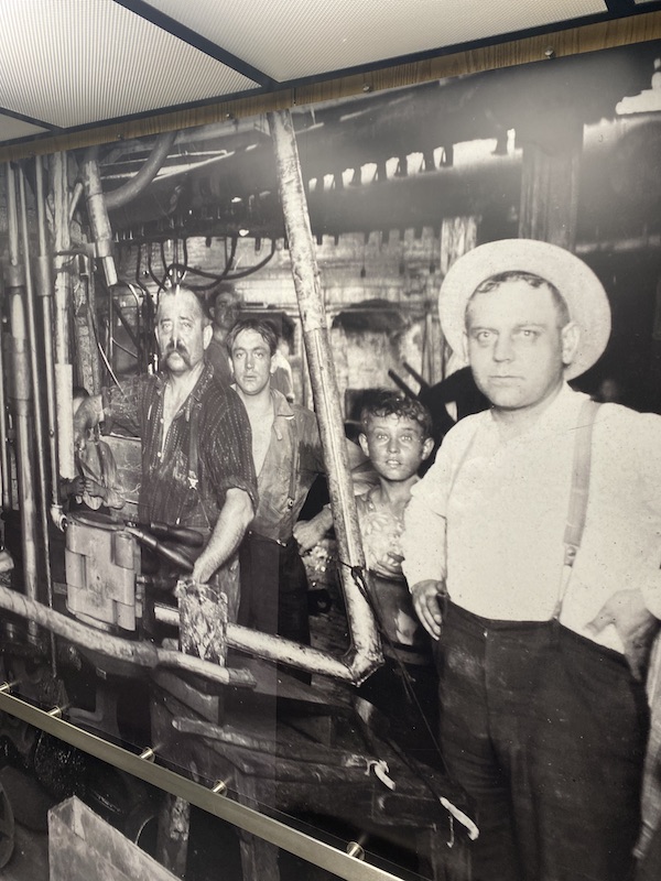 A mural showing glass workers in a glass factory in the late 1800s.